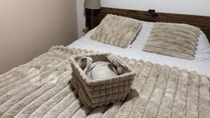 Una cama con una manta beige suave y esponjosa, un plaid a juego y una cesta beige pequeña.
