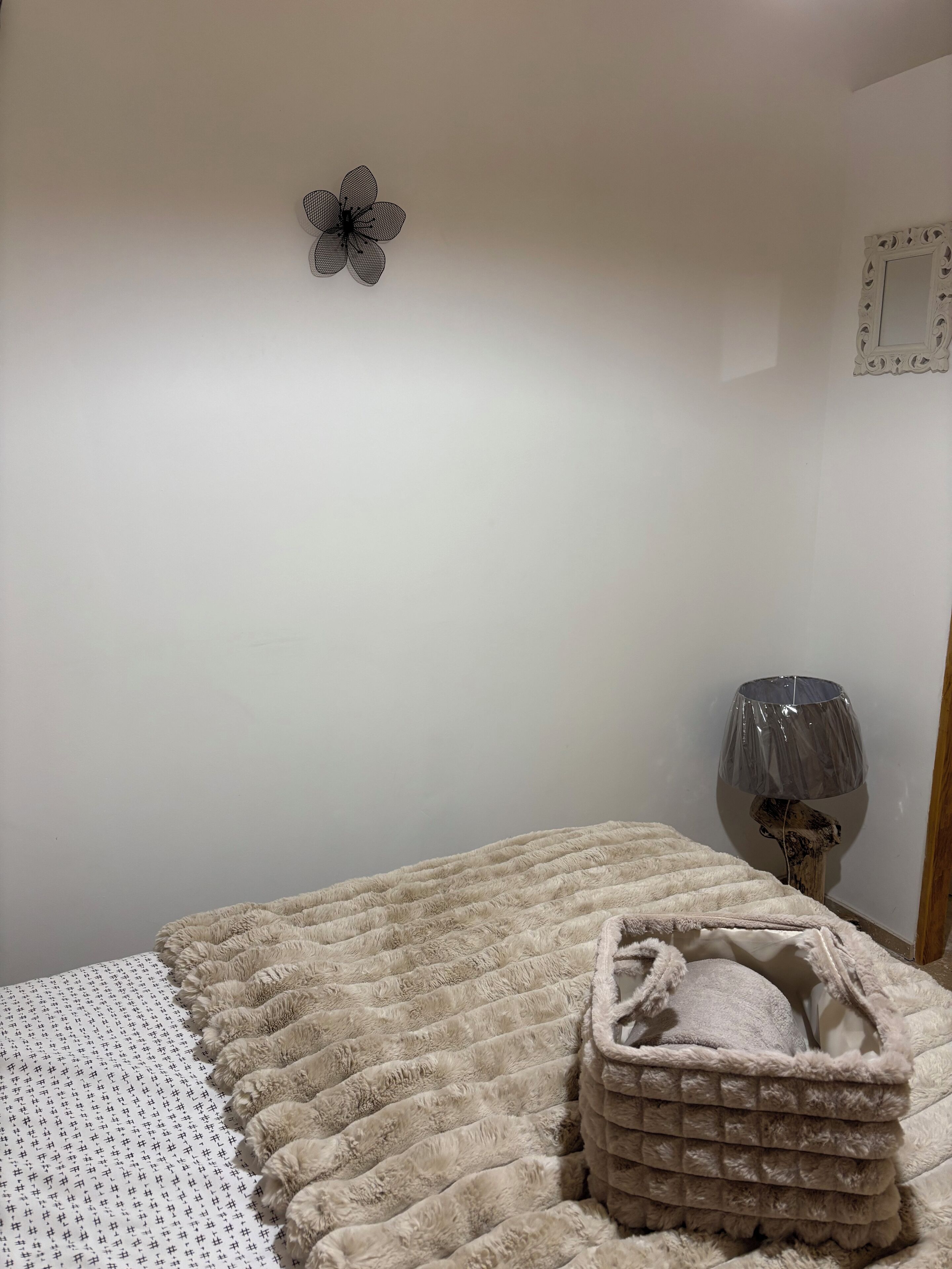 Et soveværelse med en seng, et dekorativt vægkunstværk, en lampe og et vamset tæppe.