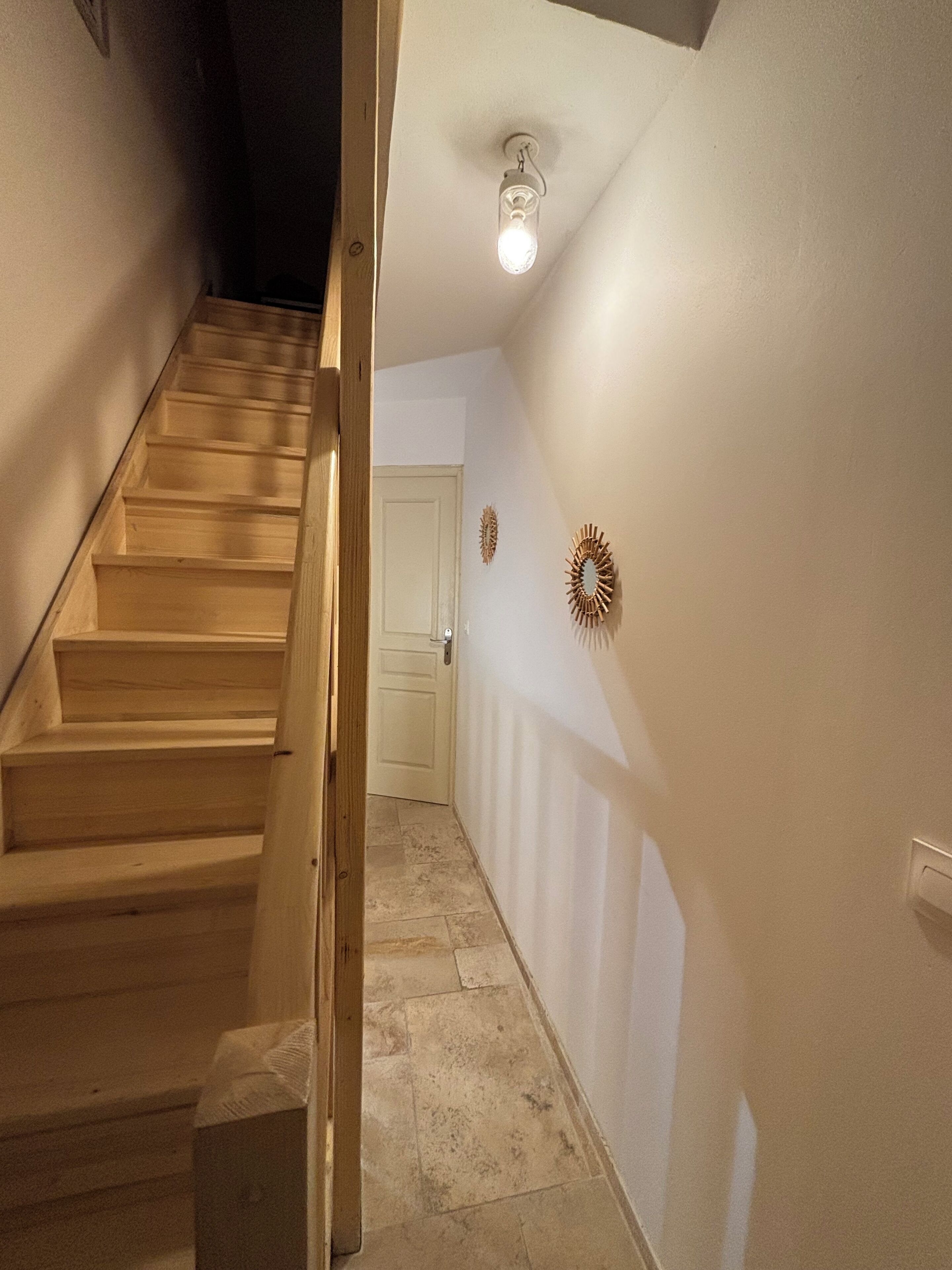 Una escalera que lleva a una puerta, con una lámpara arriba y dos adornos en la pared.