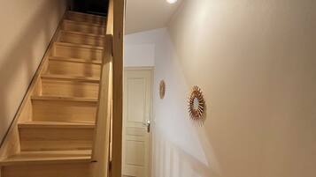 Una escalera que lleva a una puerta, con una lámpara arriba y dos adornos en la pared.