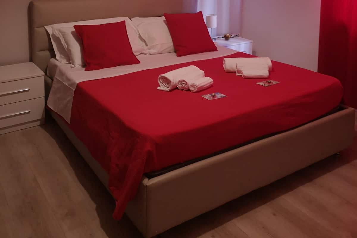 A neatly made bed with red and white bedding, a red throw blanket, and rolled towels. There is a wall with a motivational quote.