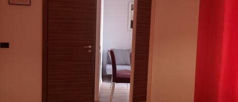 Habitación de hotel con una cama roja, una puerta de madera, una pared blanca y una lámpara en el techo.