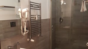 Un baño moderno con ducha de vidrio, lavamanos blanco y secador de pelo montado en la pared.