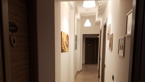 Un pasillo con suelo de madera, paredes blancas y una serie de puertas a un lado.