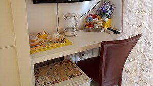 Una habitación compacta con televisión de pantalla plana en la pared, cafetera, una mesita con un mapa y una silla.