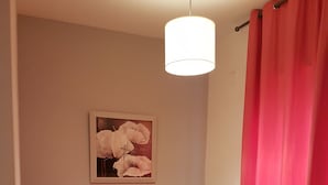 Una habitación con sofá, lámpara colgante, cuadro en la pared y cortina roja.