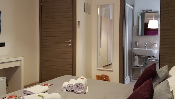 Habitación de hotel con cama, escritorio, espejo y baño visible a través de una puerta abierta.