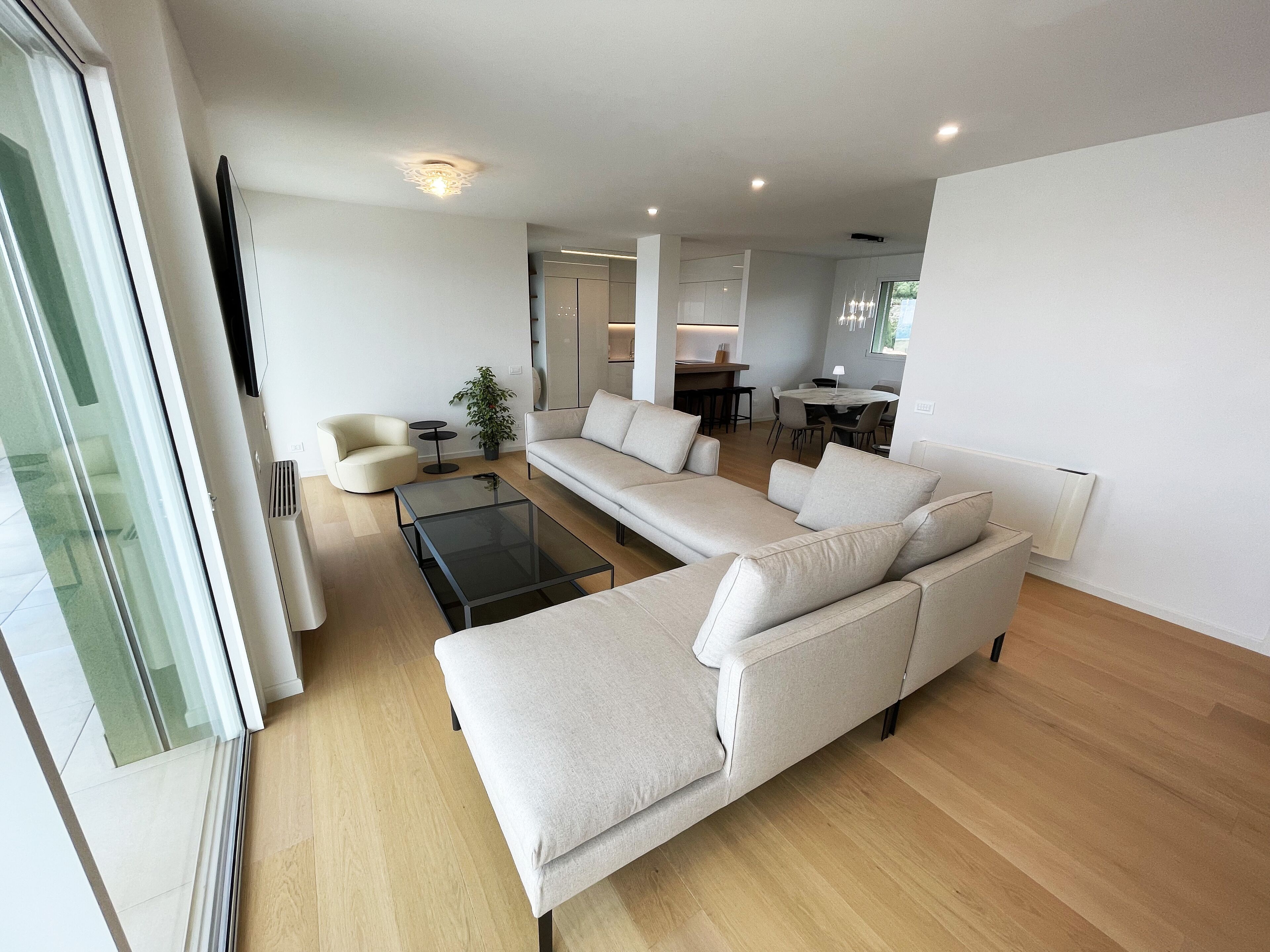 Un salon moderne avec un canapé d’angle, une table basse en verre et un coin repas à l’arrière-plan.