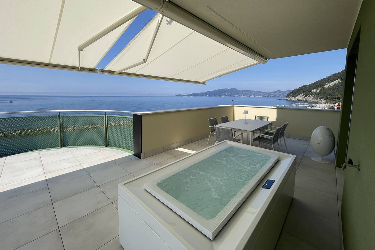 A balcony with a view of the sea, a table with chairs, and a hot tub.