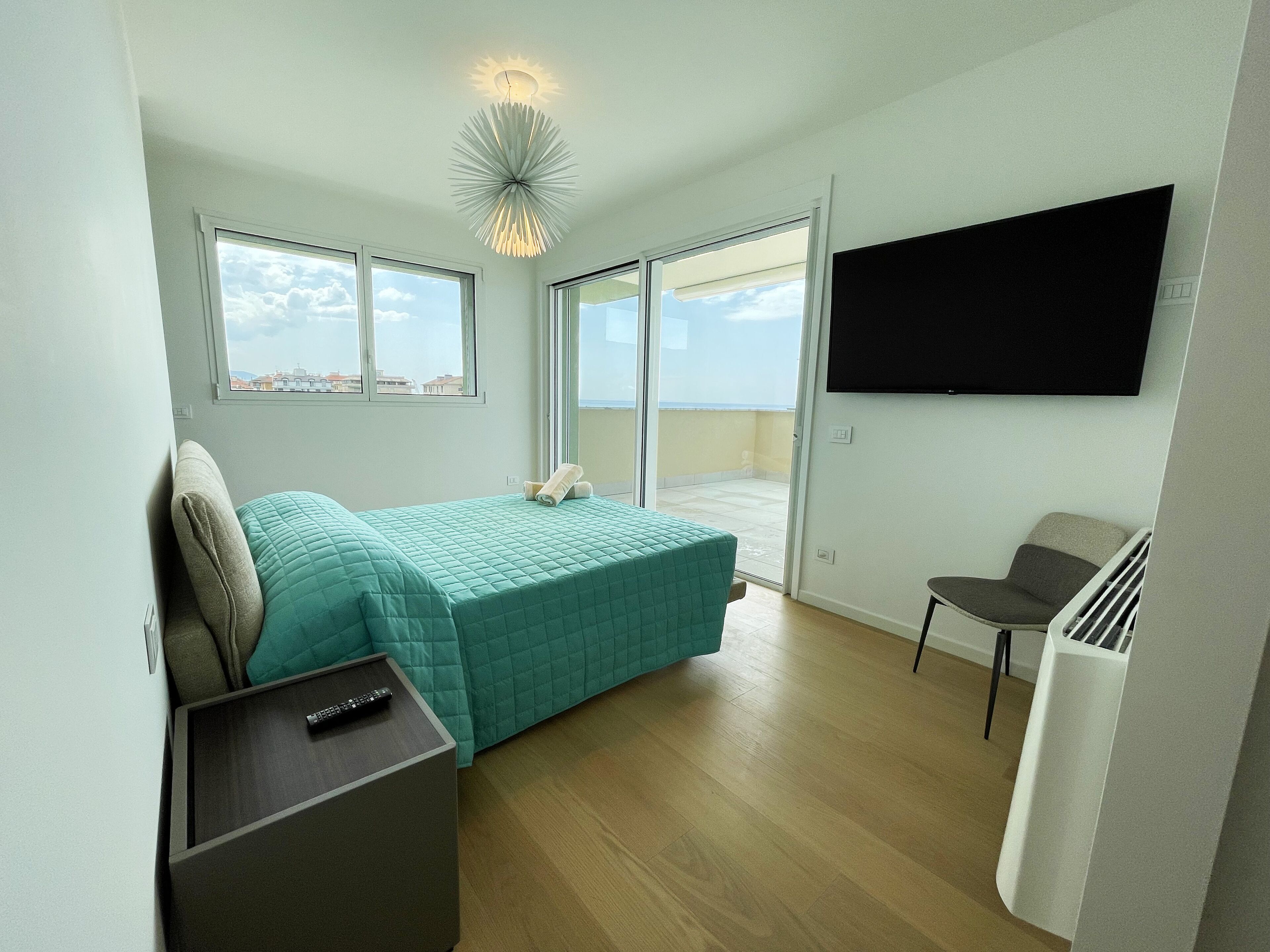 A bedroom with a bed, a TV, a chair, and a balcony with a view.