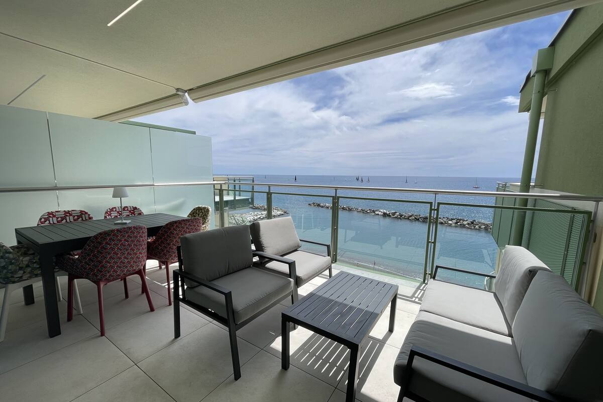 A balcony with a view of the sea, furnished with a table, chairs, and a sofa.