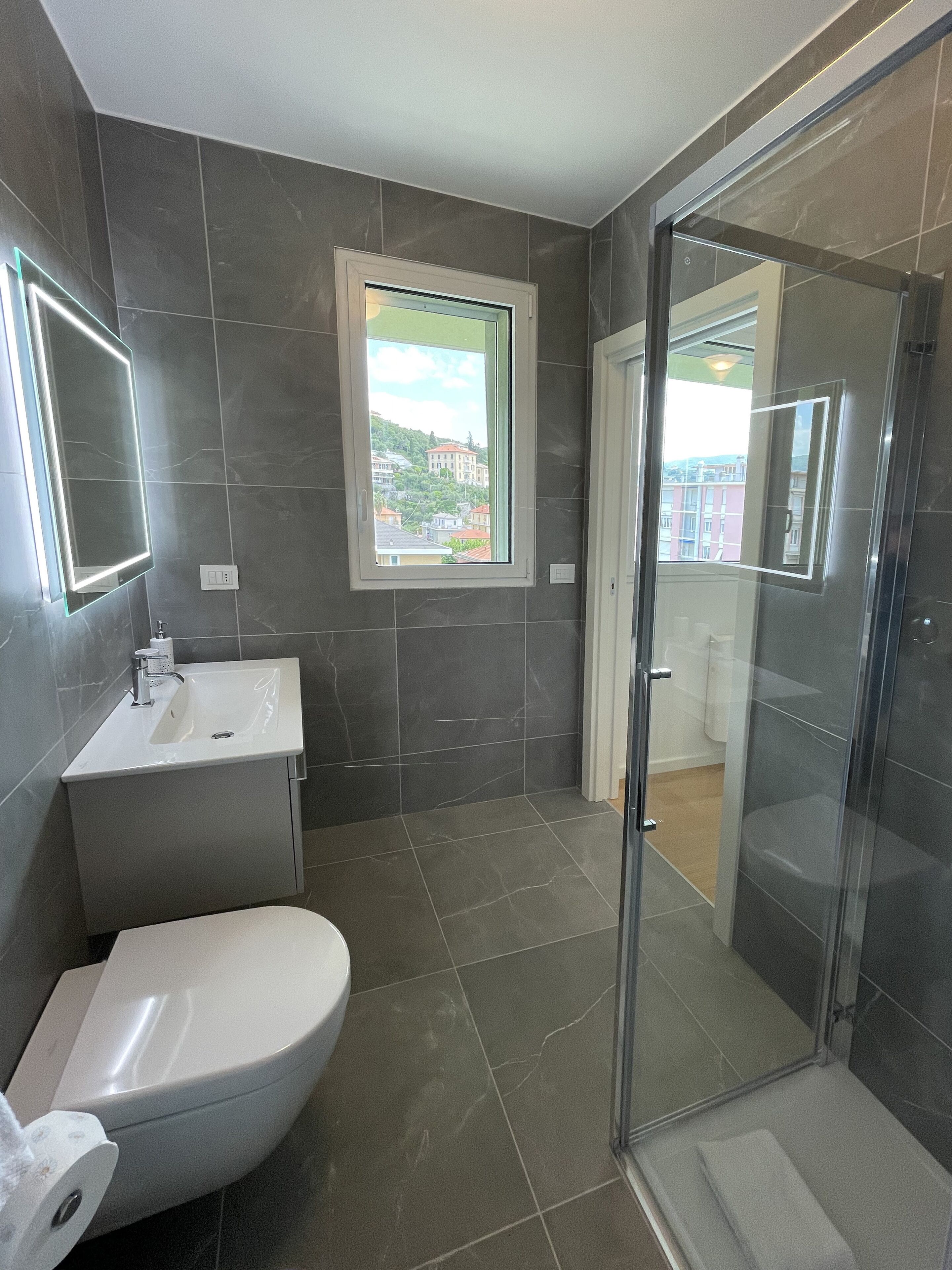 Un baño moderno con inodoro, lavamanos y cabina de ducha con mampara de vidrio.
