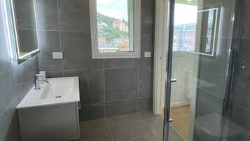 Un baño moderno con inodoro, lavamanos y cabina de ducha con mampara de vidrio.