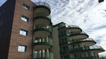 A multi-story building with a modern architectural design, featuring balconies with glass railings and a mix of window styles.