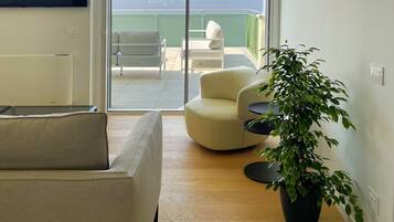 A modern living room with a sofa, a potted plant, and a view of a balcony with outdoor furniture.