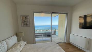 A bedroom with a large bed, a sliding glass door to a balcony, a mounted TV, and a ceiling light.