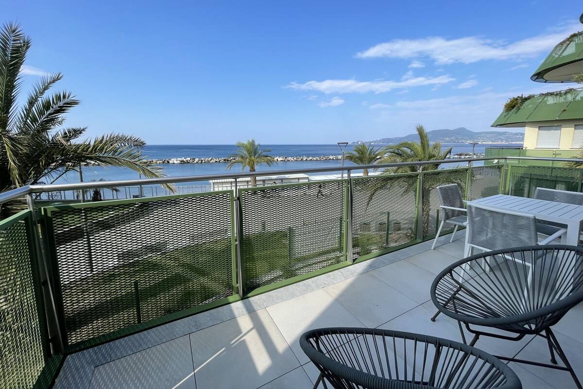 A balcony with a view of the sea, equipped with metal chairs and a table.