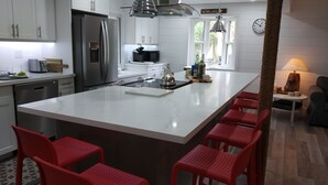 A modern kitchen with a large island, stainless steel appliances, and red bar stools. -  The Lazy Acre: Waterfront cottage with unparalleled views of Smith's Bay. (Prince Edward)