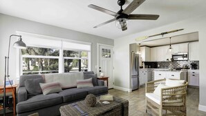 A modern living room with a grey sofa, wicker ottoman, and a ceiling fan.