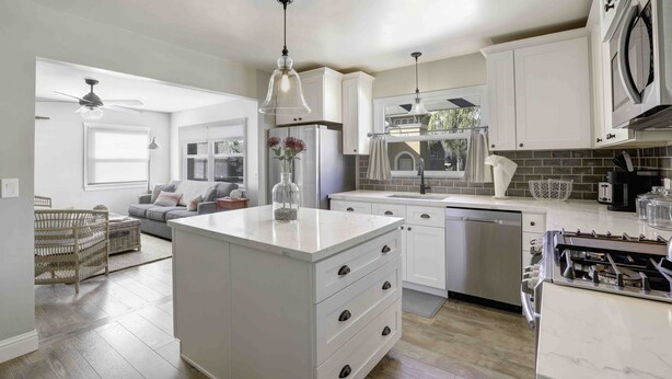 A modern kitchen with white cabinetry, a central island with drawers, stainless steel appliances, and pendant lighting.