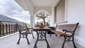 Une terrasse extérieure avec une table et deux bancs, un pot de fleurs et une vue sur un arbre et des montagnes.