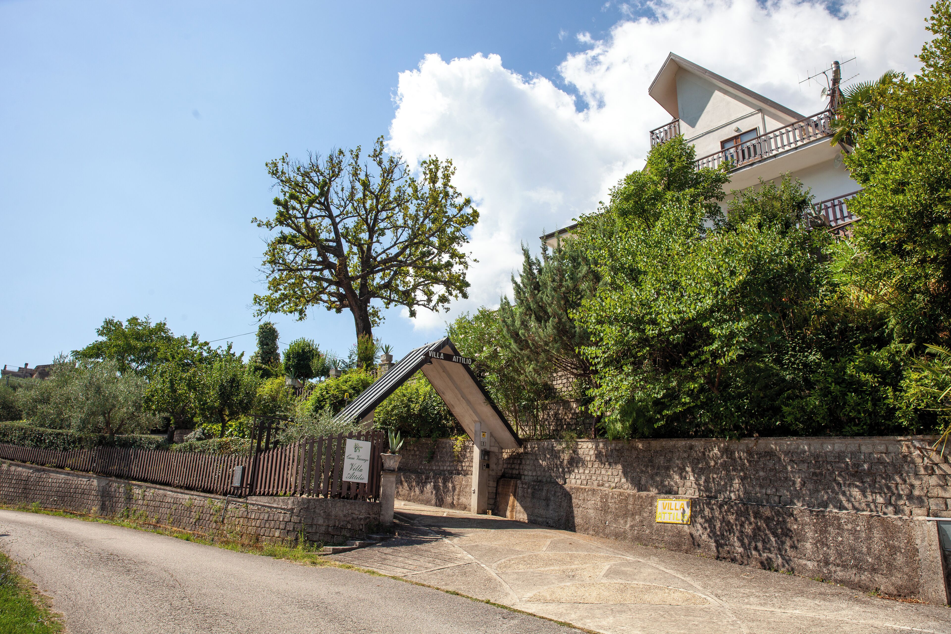 A villa with a stone wall entrance, a balcony, and a view of the surrounding greenery.