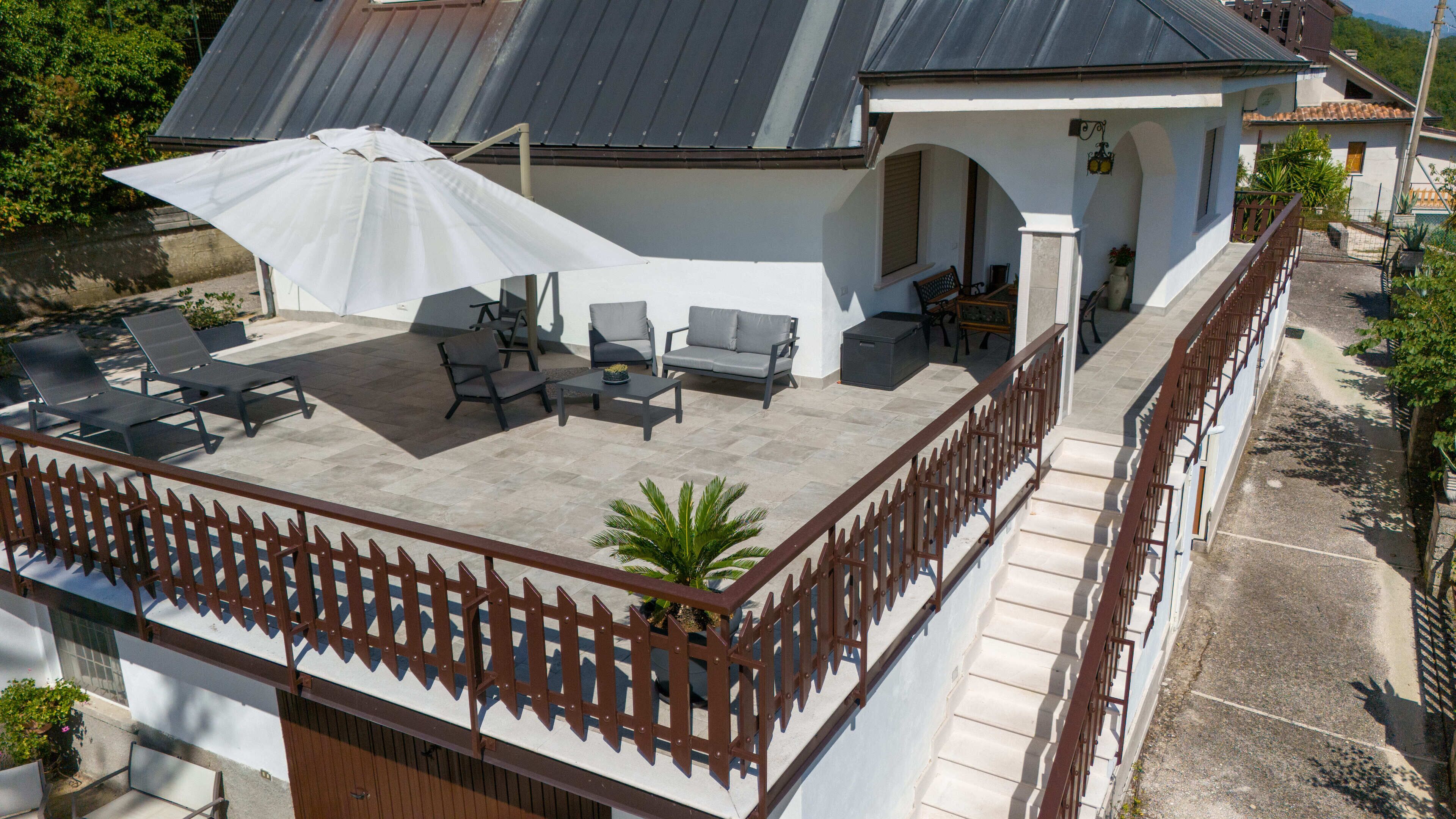 Un patio en la azotea con mobiliario exterior, una zona cubierta y una escalera que lleva al nivel superior.