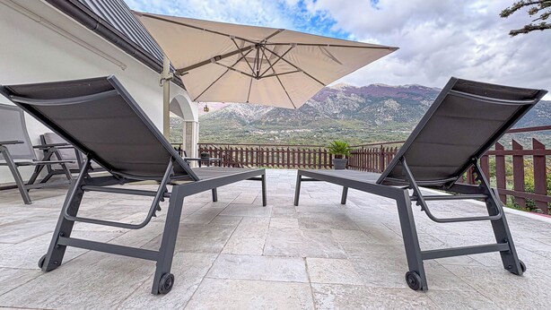Een terras met twee loungestoelen en een grote parasol, met uitzicht op een bergachtig landschap.