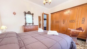 Une chambre à coucher avec un grand lit, une armoire en bois, une commode, un miroir et un lustre.