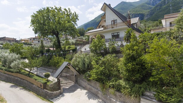 Une villa avec un mur en pierre, une clôture en bois et une végétation luxuriante.