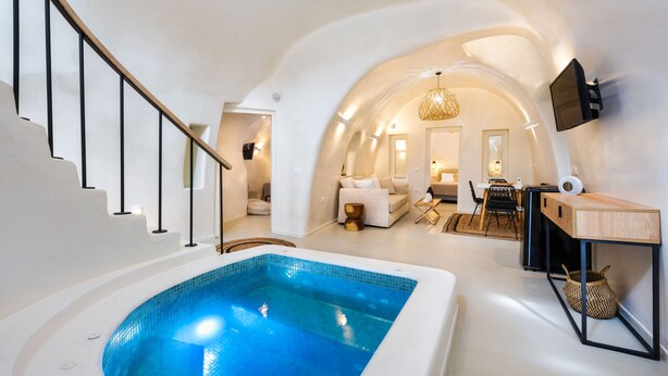 A modern interior with a swimming pool, a staircase, and a cozy living area with a sofa and a TV mounted on the wall. - Hill Suites (Santorini)