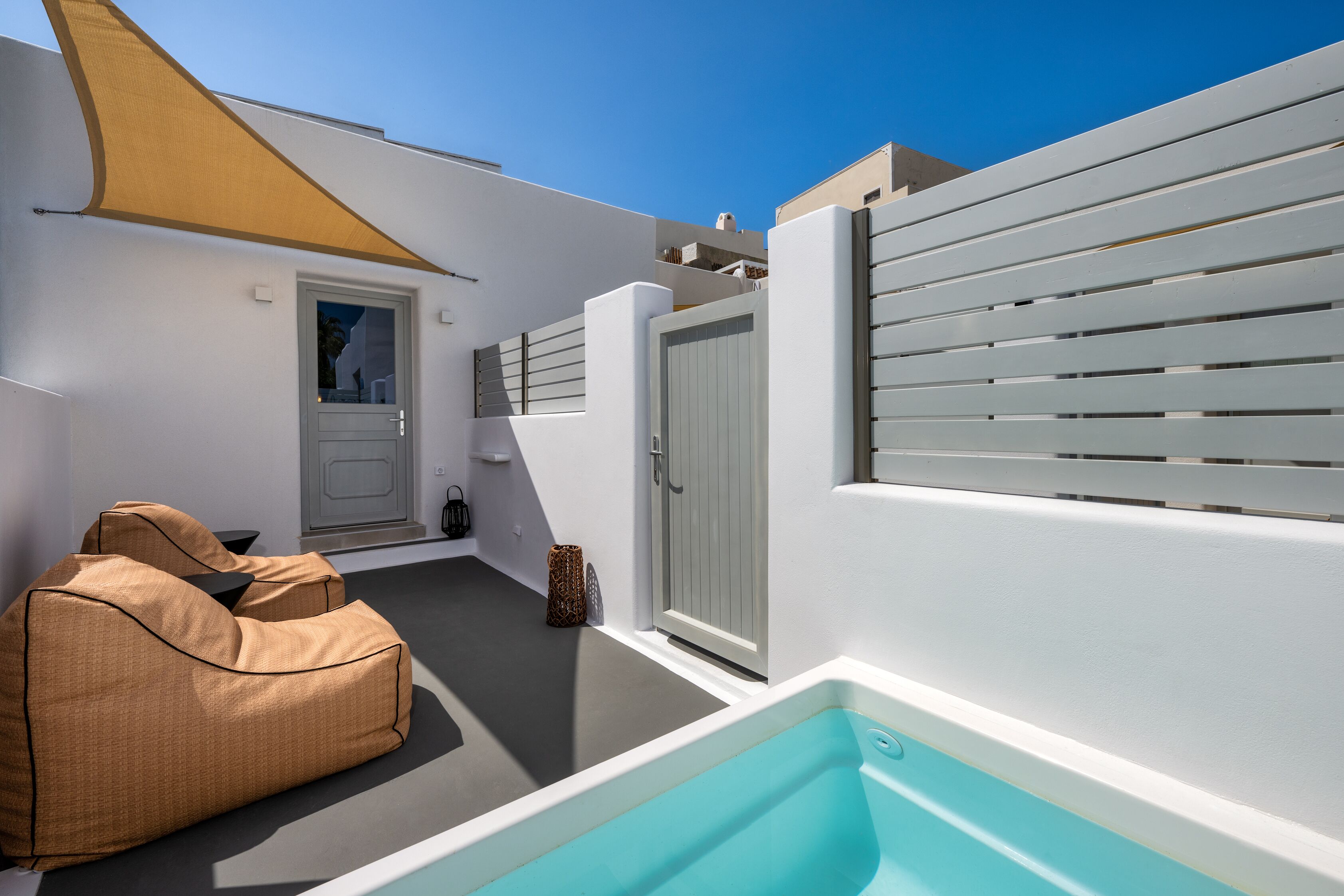 A modern outdoor space with a pool, a seating area, and a door leading to a covered entrance.