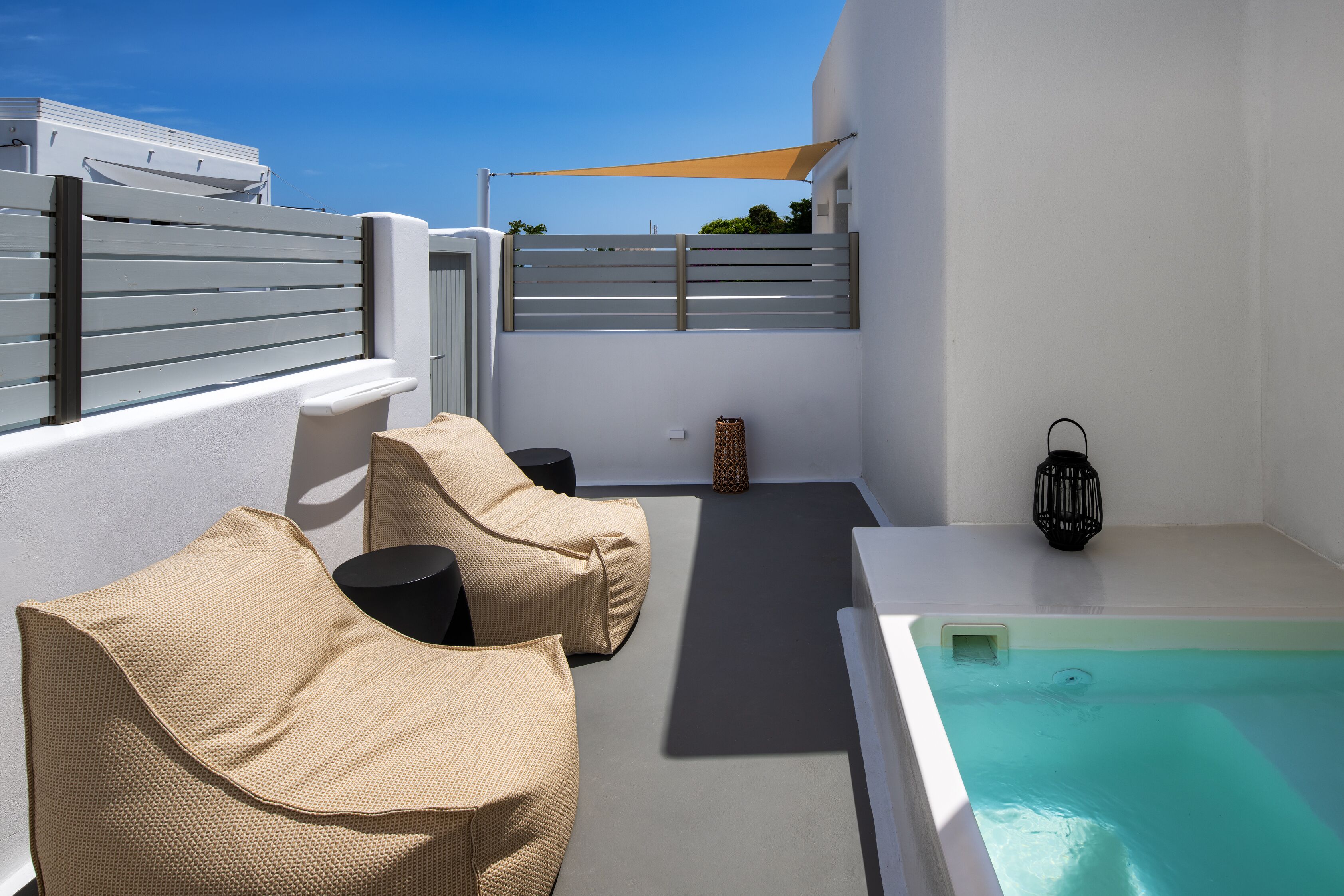 Terraza en la azotea con piscina, paredes blancas y dos sillones color beige.