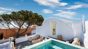 A rooftop pool area with a white wall, a tree, and a view of the sky.