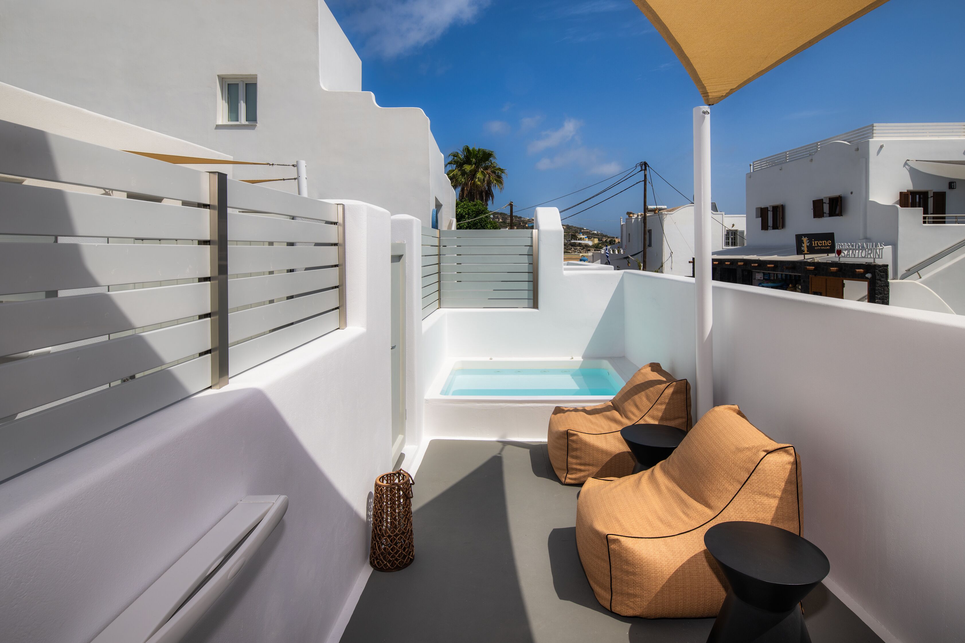 A rooftop terrace with a pool, white walls, and beige seating.