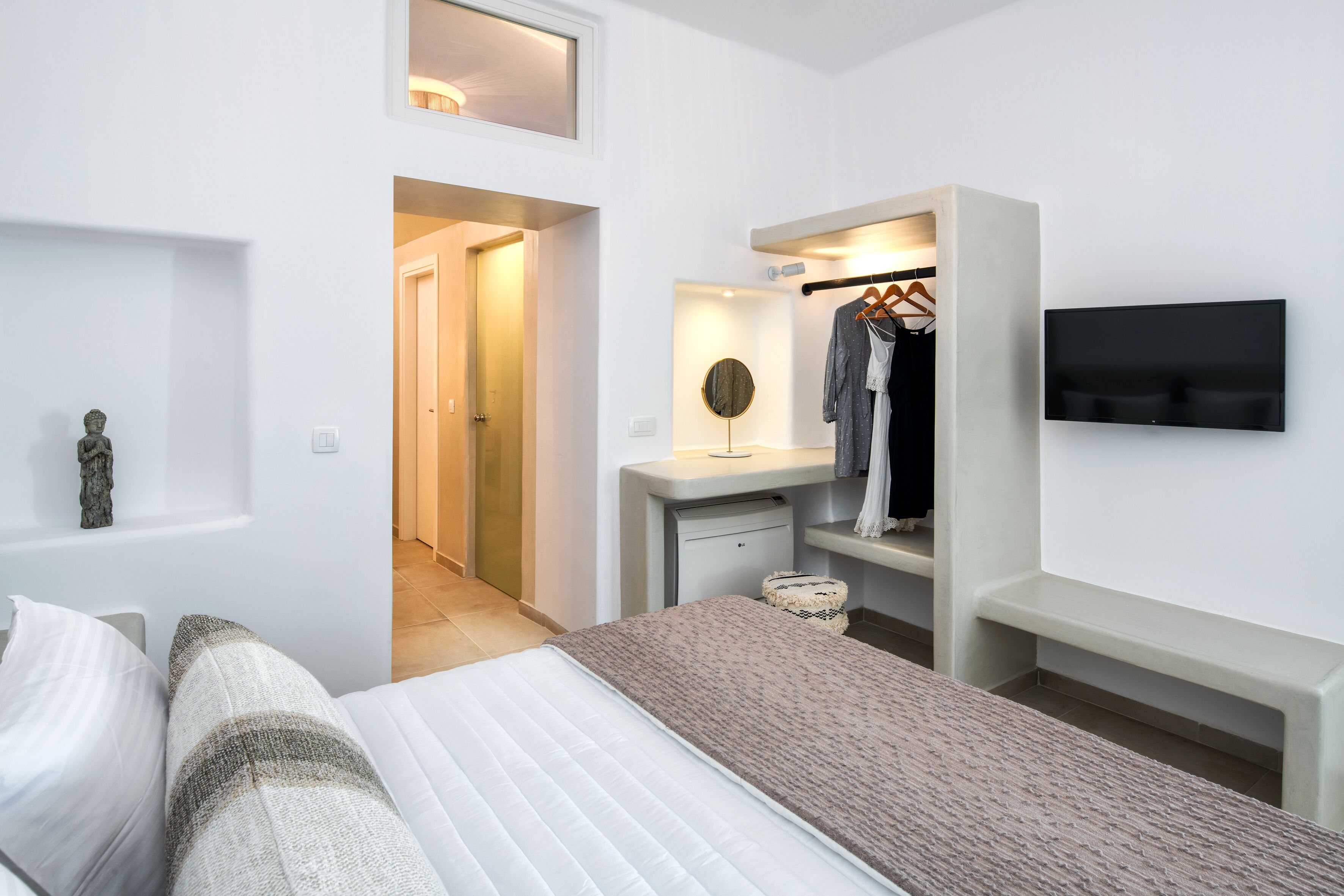 Une chambre moderne avec un lit, une coiffeuse avec un miroir, un téléviseur fixé au mur et un dressing.
