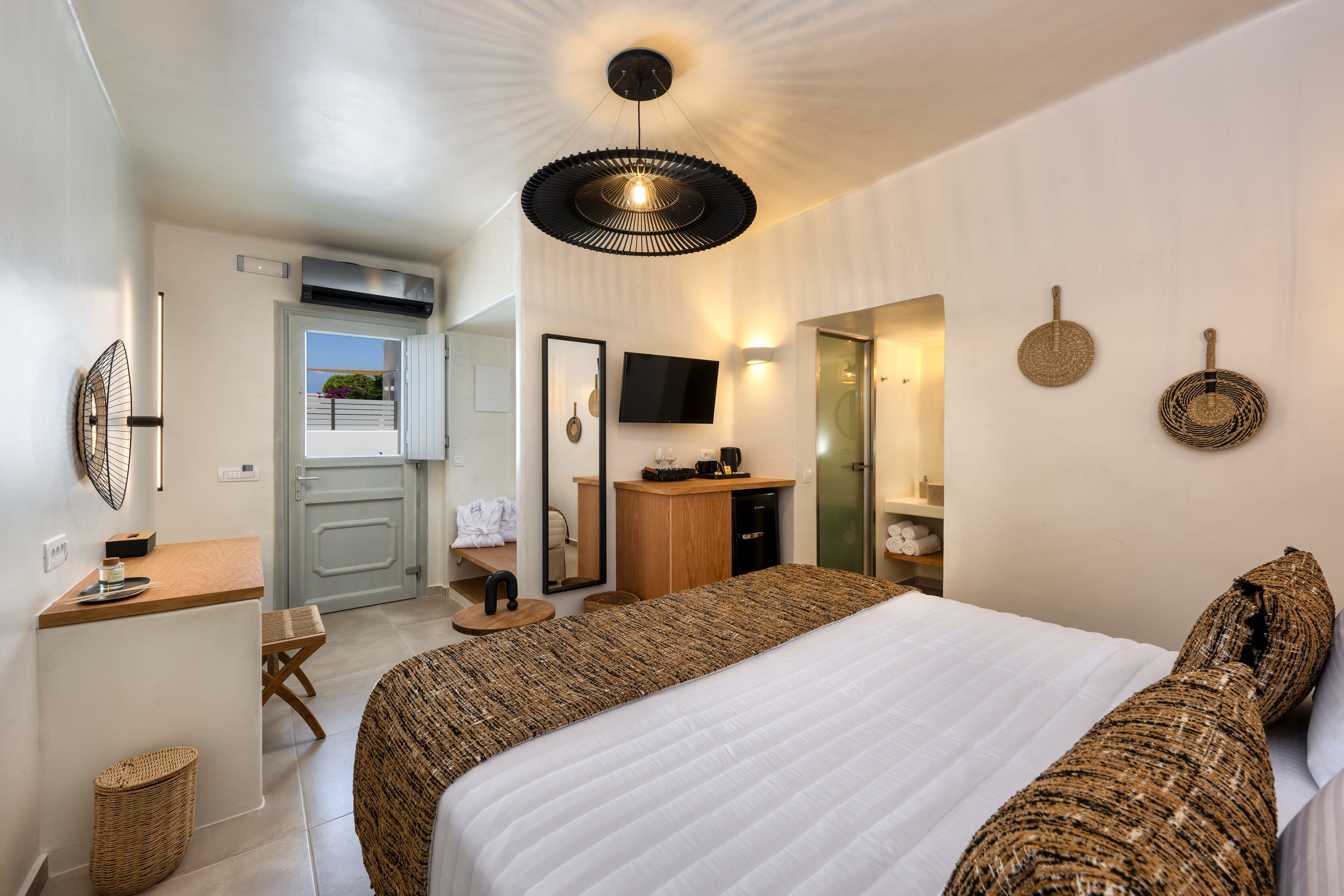 A modern hotel room with a large bed, a desk, a chair, a television, and a bathroom.