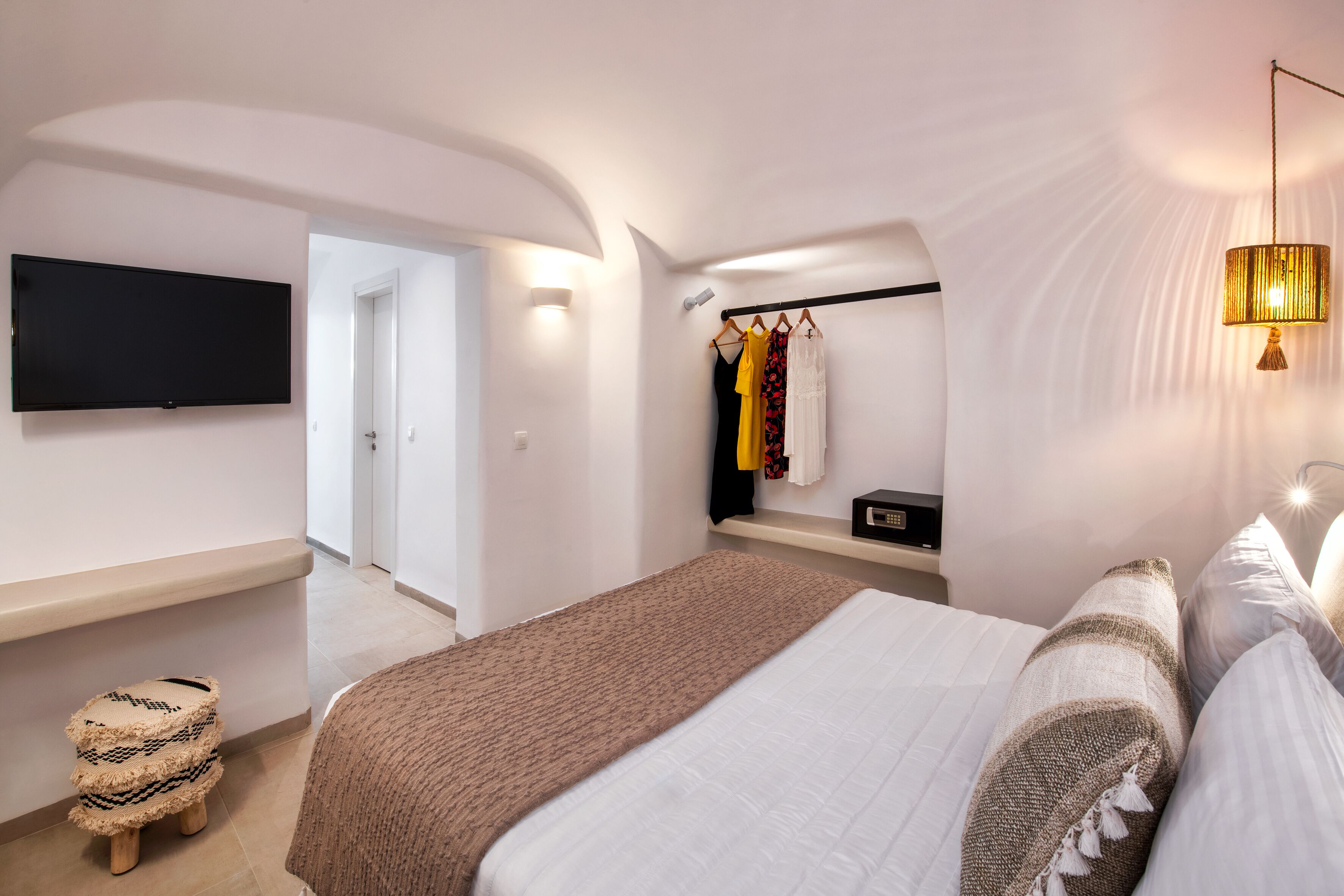 A modern bedroom with a large bed, a flat-screen TV, a bedside table, a hanging light fixture, and a wardrobe.