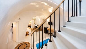 A modern interior with a white staircase, a wooden railing, and a blue pool area. - Hill Suites (Santorini)