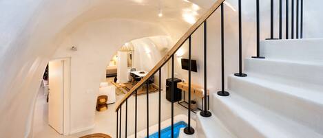 Un interior moderno con una escalera blanca, barandilla de madera y zona de piscina azul.