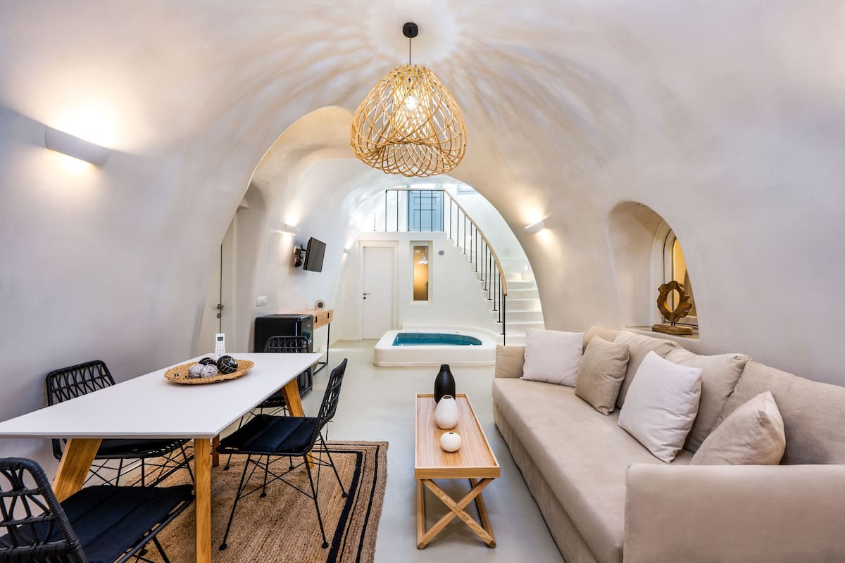 Ein modernes Interieur mit einem weißen Esstisch, schwarzen Stühlen, einem beigen Sofa und einem Holztisch. Eine Treppe führt zu einem Balkon mit Blick.