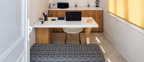 A compact workspace with a white desk, a laptop, a printer, and a hanging light fixture.