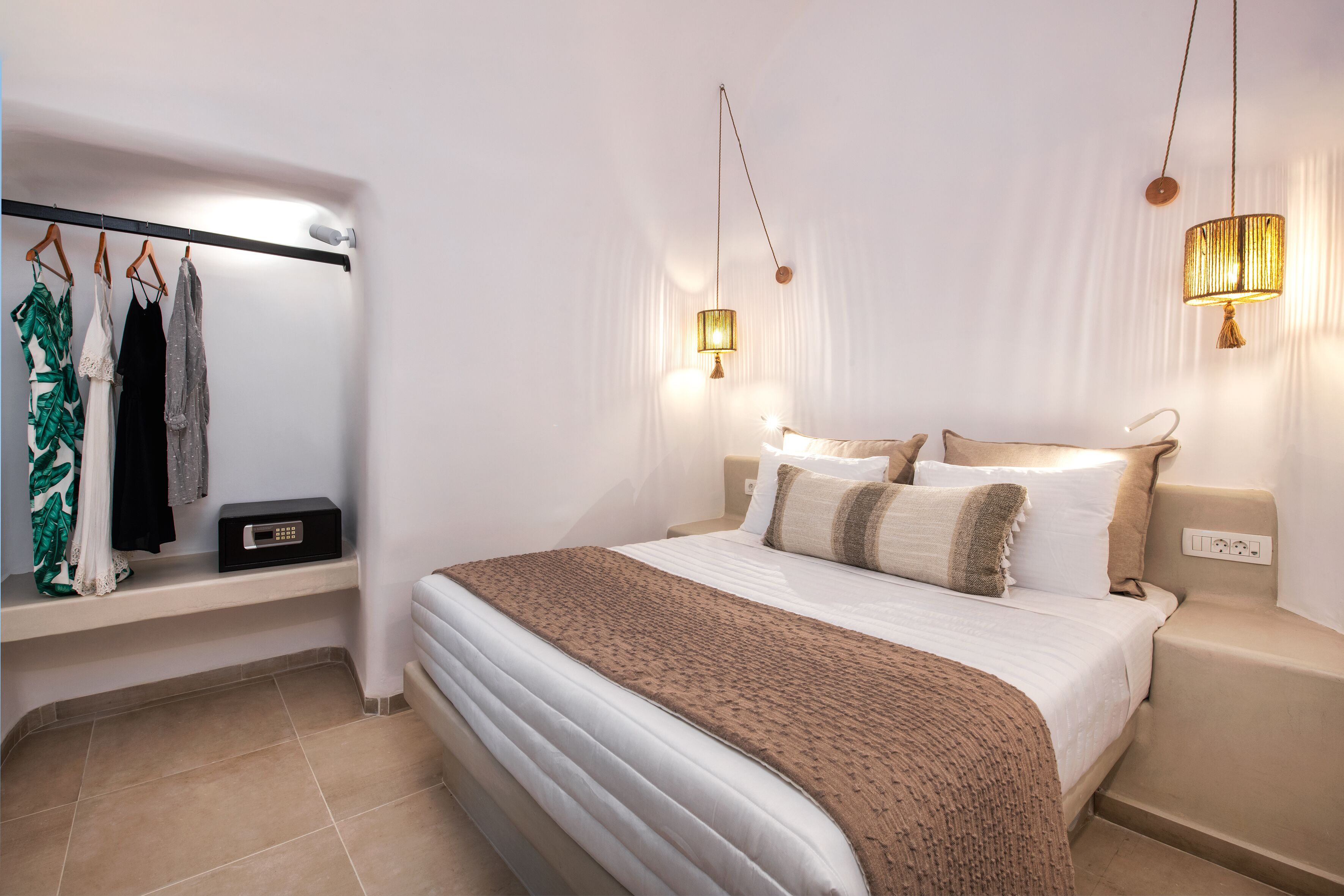 Un dormitorio ordenado con cama, mesitas de noche, una lámpara colgante y un perchero.