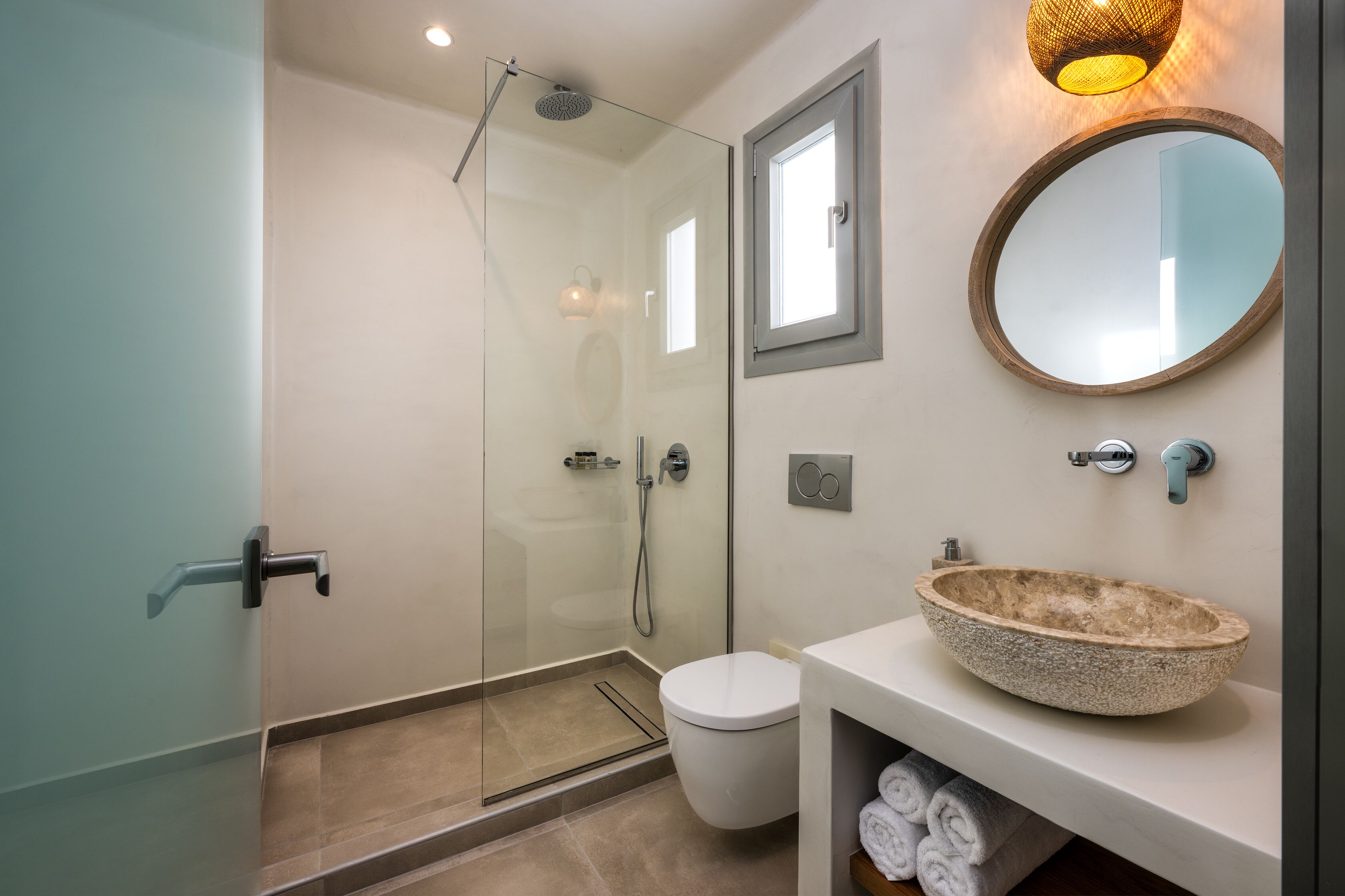 Un bagno moderno con box doccia in vetro, un WC bianco, uno specchio rotondo e un lavabo con bacino in pietra.