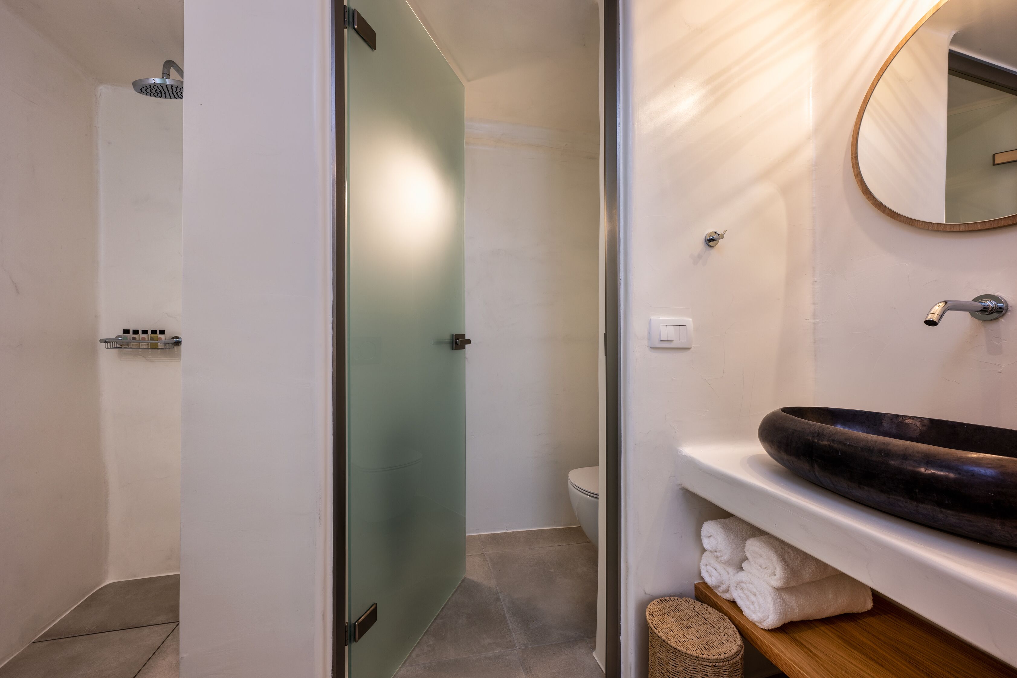 A modern bathroom with a glass shower enclosure, a round sink with a dark basin, and neatly folded towels on a shelf.