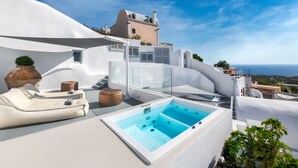 A rooftop with a hot tub, lounge chairs, and a view of the sea. - Hill Suites (Santorini)