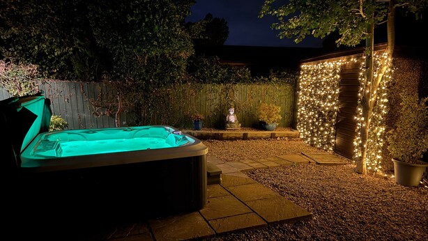 Un jacuzzi en un jardín con valla de madera y plantas en macetas.
