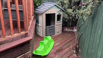En træterrasse med et lille legeskjul og en grøn slæde.
