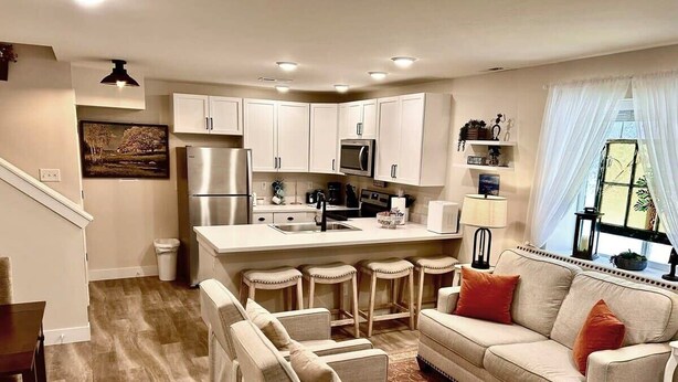 A modern kitchen with white cabinets, a stainless steel refrigerator, and a bar area with stools.