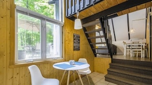 Una habitación acogedora con paredes de madera, una mesa de comedor con sillas, una escalera y vistas al exterior.